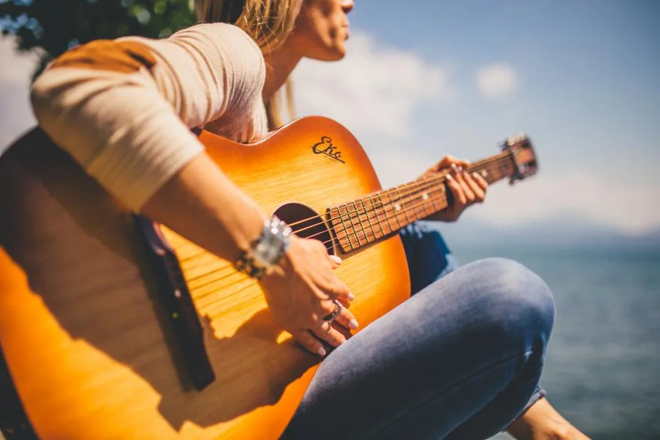 A teenager playing an acoustic guitar in warm sunlight